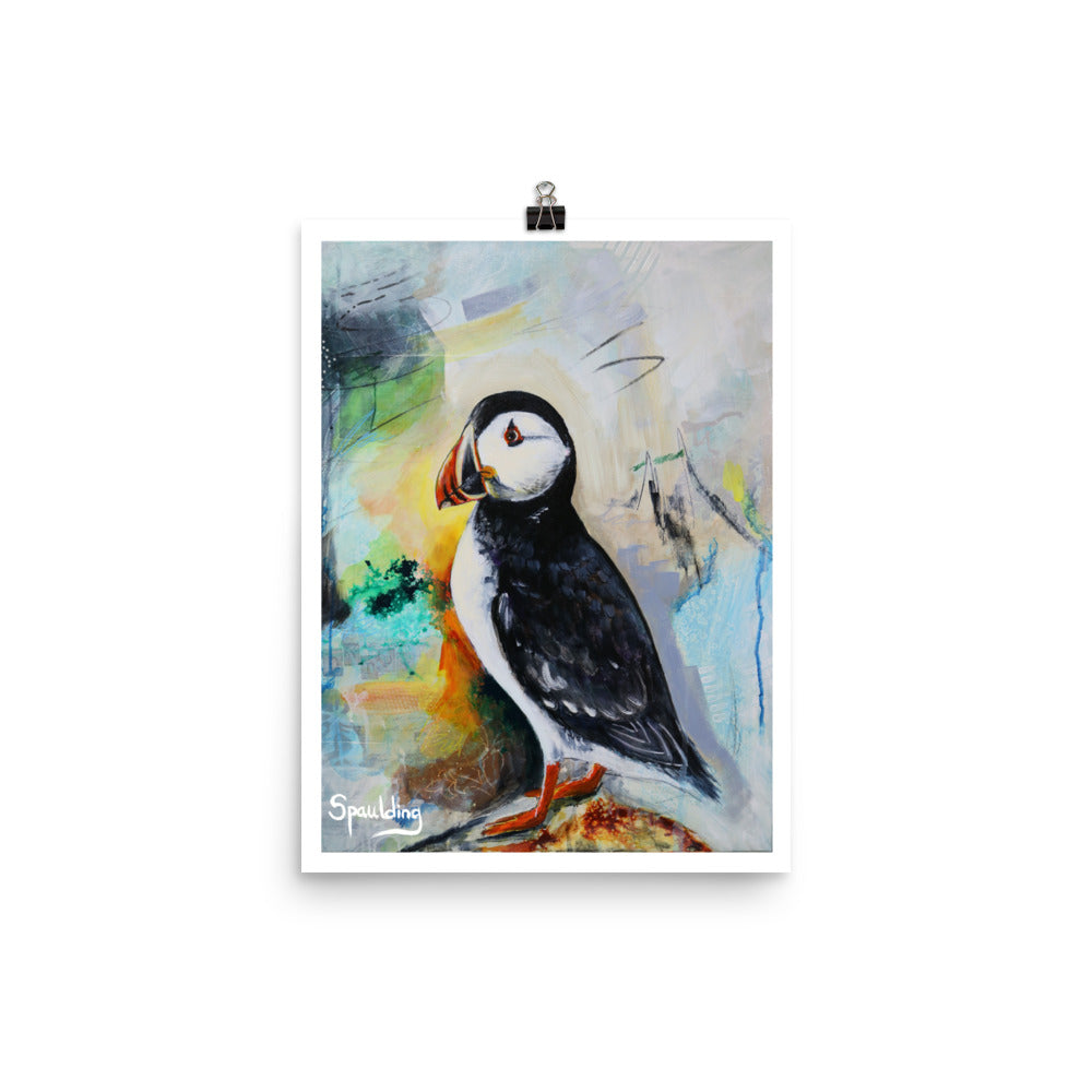 Paper art print of a black and white puffin bird with an orange beak and feet. The background colors are grey, green, yellow,blues and black.