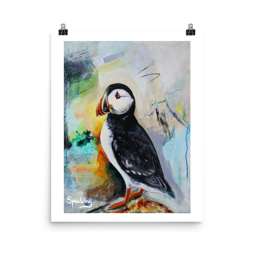 Paper art print of a black and white puffin bird with an orange beak and feet. The background colors are grey, green, yellow,blues and black.