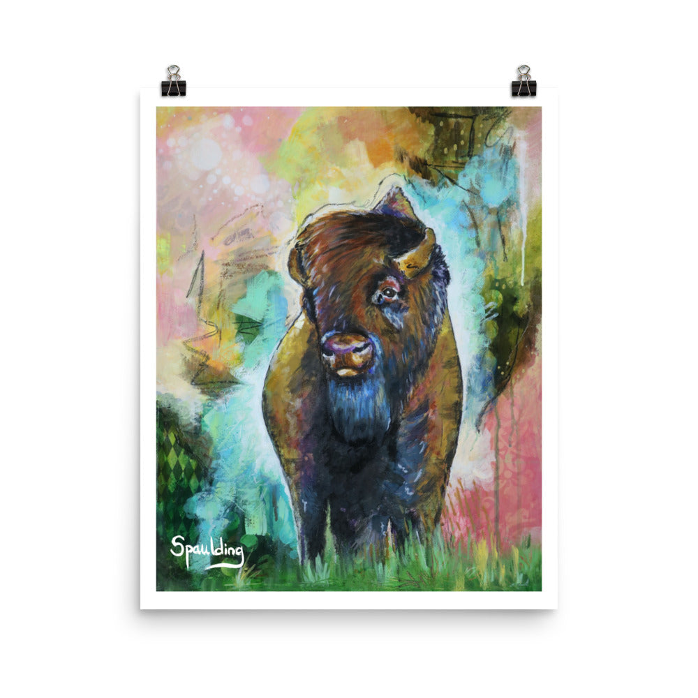 Paper art print of a bison standing in green grass with a background of pinks, yellows, orange, teal and greens.