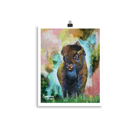Paper art print of a bison standing in green grass with a background of pinks, yellows, orange, teal and greens.
